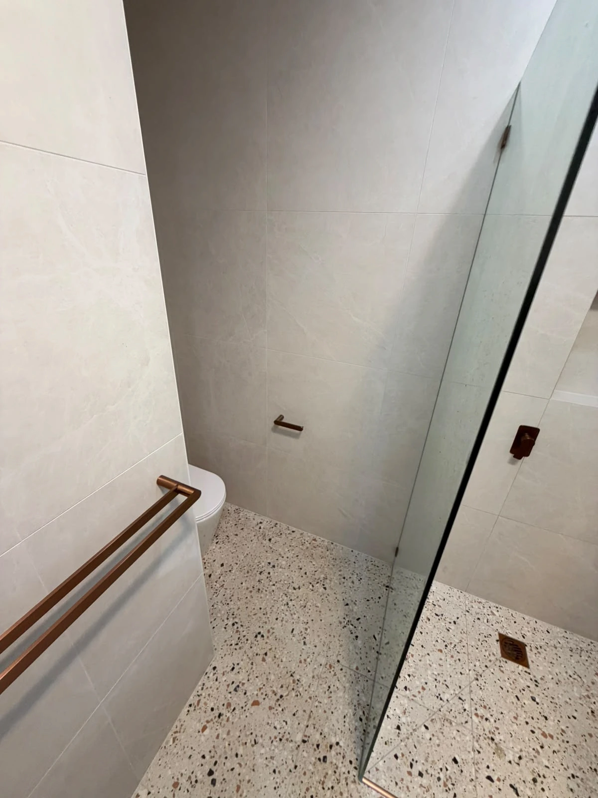 Terrazzo-look bathroom floor, shower drainage and frameless glass in the finished bathroom